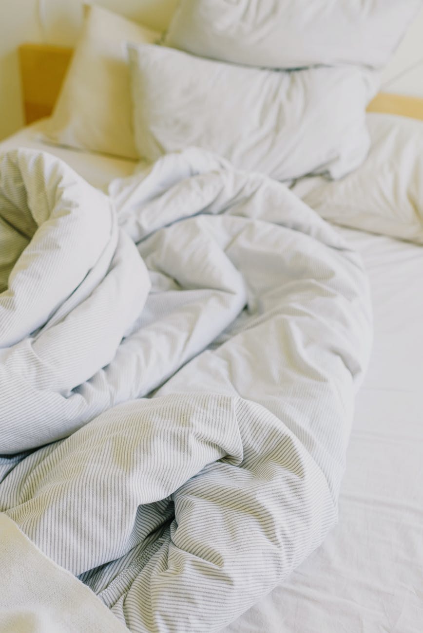 messy soft bed with pillows and blanket in daylight