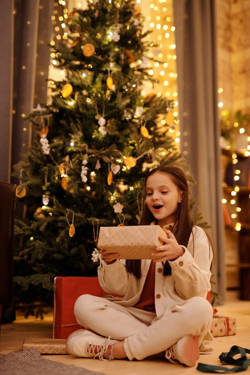 excited girl with gift box near christmas tree at home