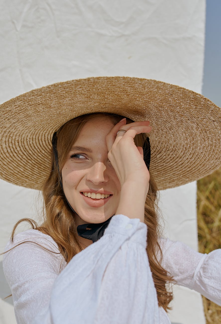 cheerful woman in hat standing near white sheet in countryside
