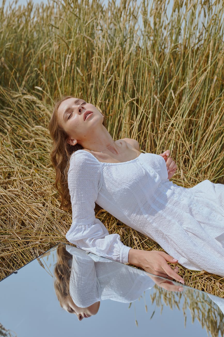 sensual woman lying on grassy meadow near mirror